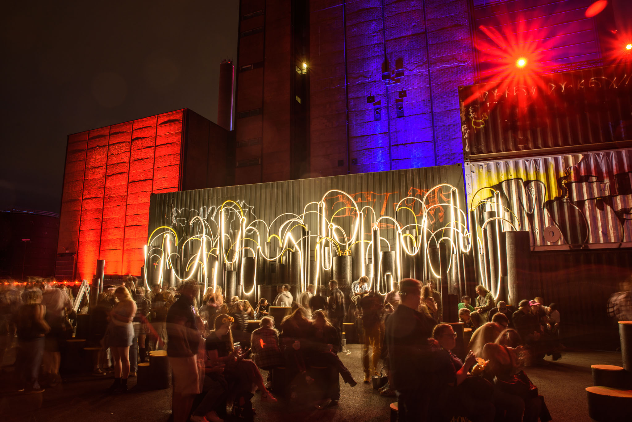 White neon tube sculptures glowing in front of red-lit cube structures at Flow Festival at night