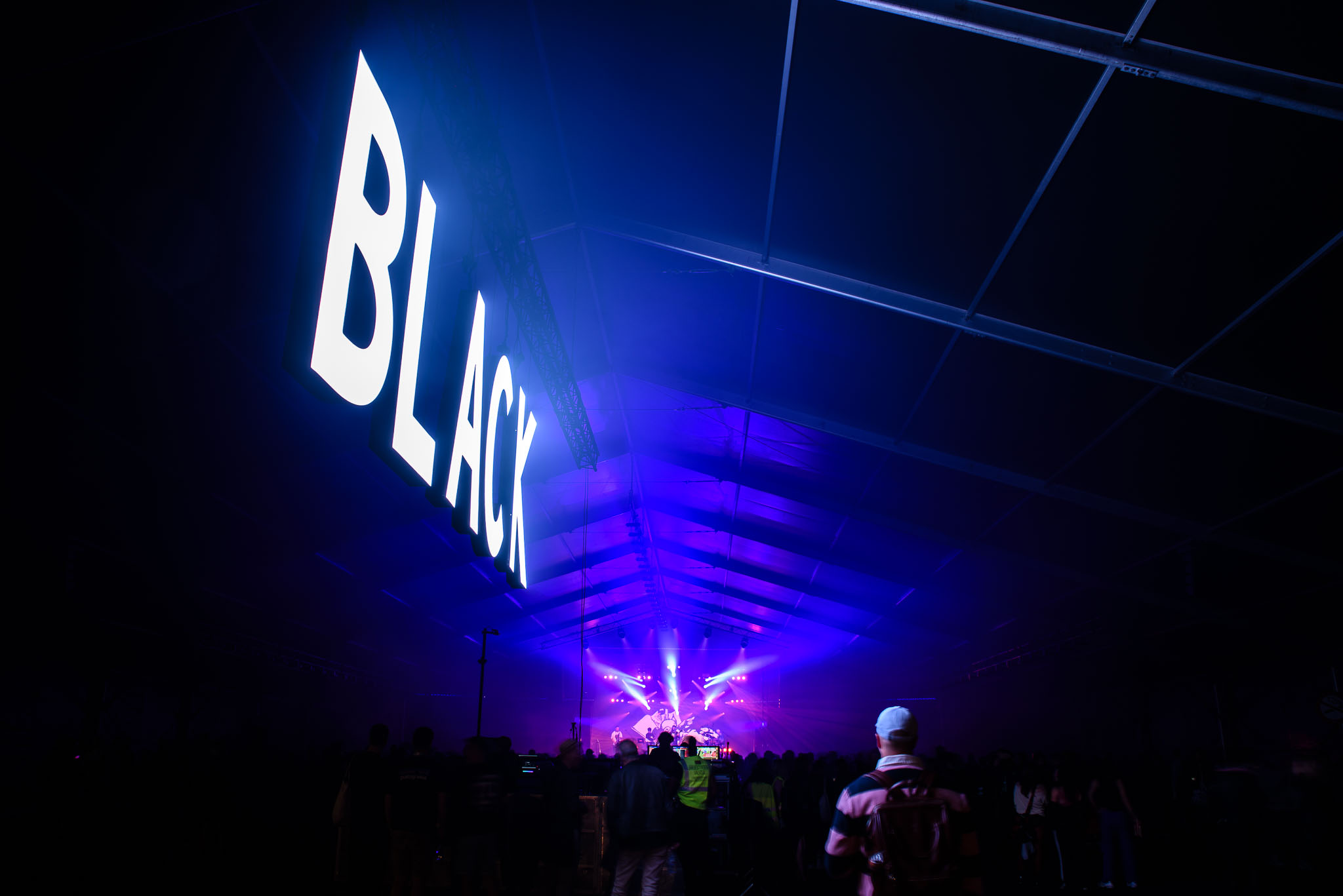 Illuminated ‘BLACK’ sign of Flow Festival’s Black Tent stage lit blue with beams over the crowd