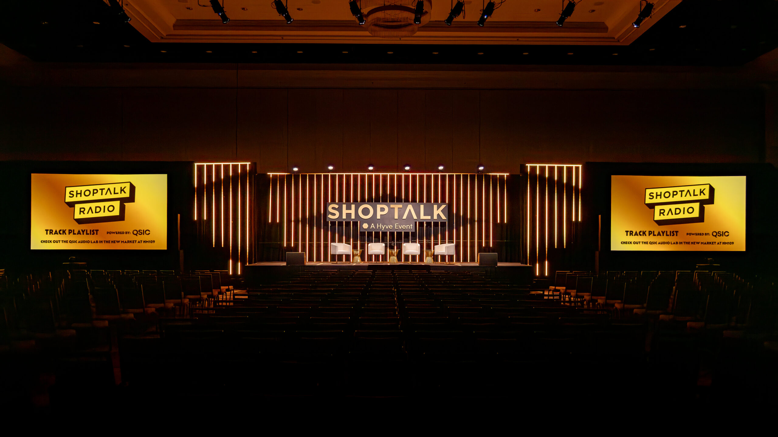Shoptalk stage with warm gold vertical light strips and side screens reading ‘SHOPTALK RADIO’ in a darkened auditorium