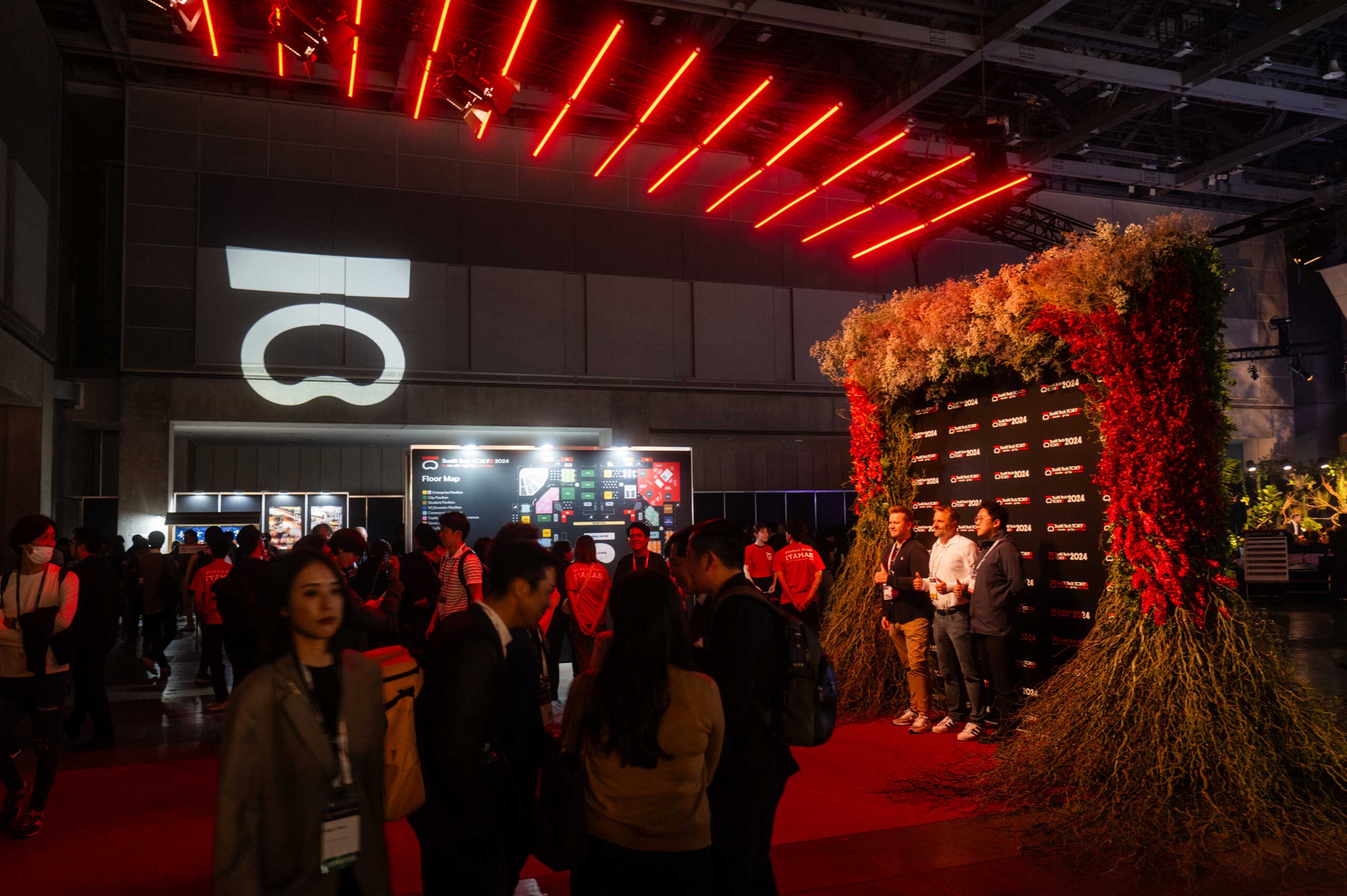 SusHi Tech expo hall with the event’s ‘S’ logo, a living plant wall and red overhead light strips as attendees mingle