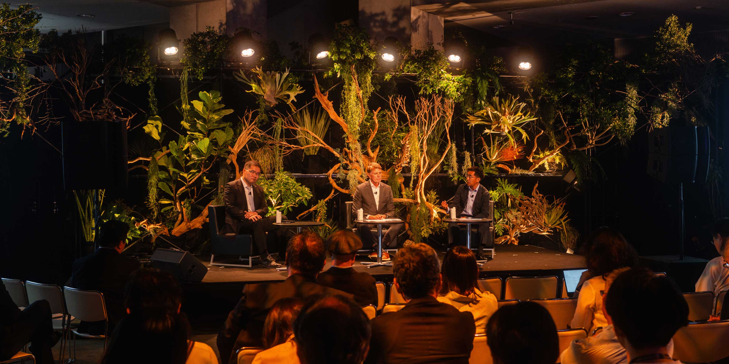 Fireside-chat stage at SusHi Tech dressed with trees and plants, three people seated in a natural, organic setting