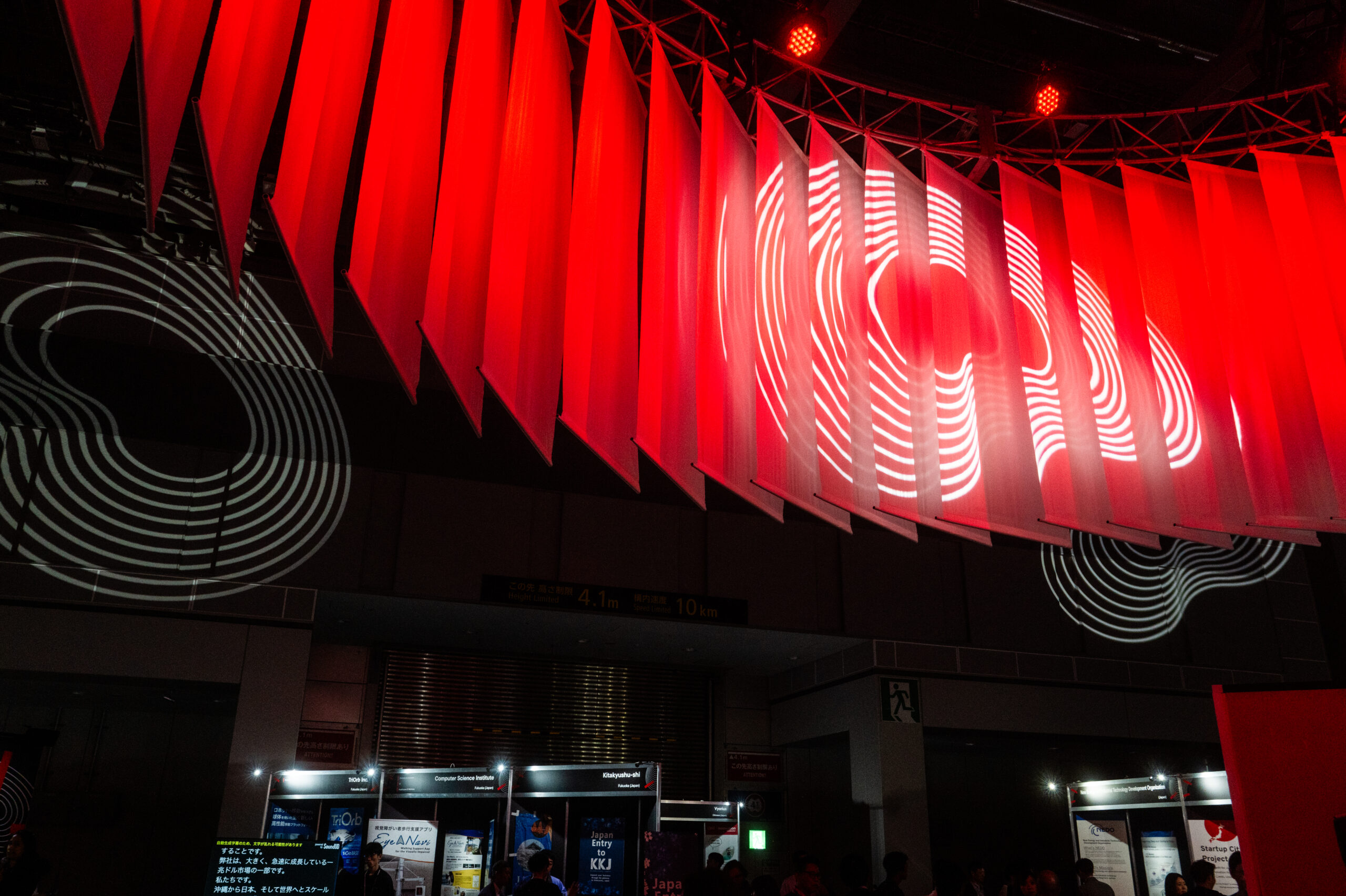 Red angular hanging panels with white spiral graphics installed above the SusHi Tech venue, echoing traditional Japanese decoration