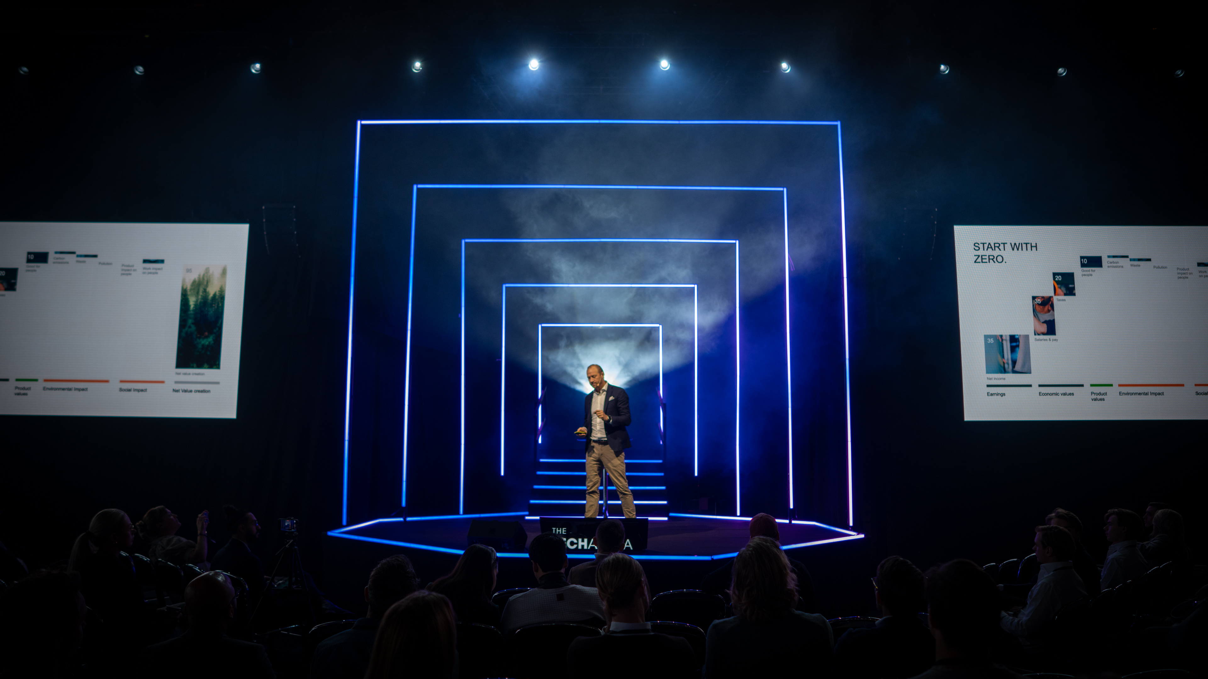 Tech Arena stage framed by concentric neon-blue light rectangles forming a glowing tunnel around a single speaker