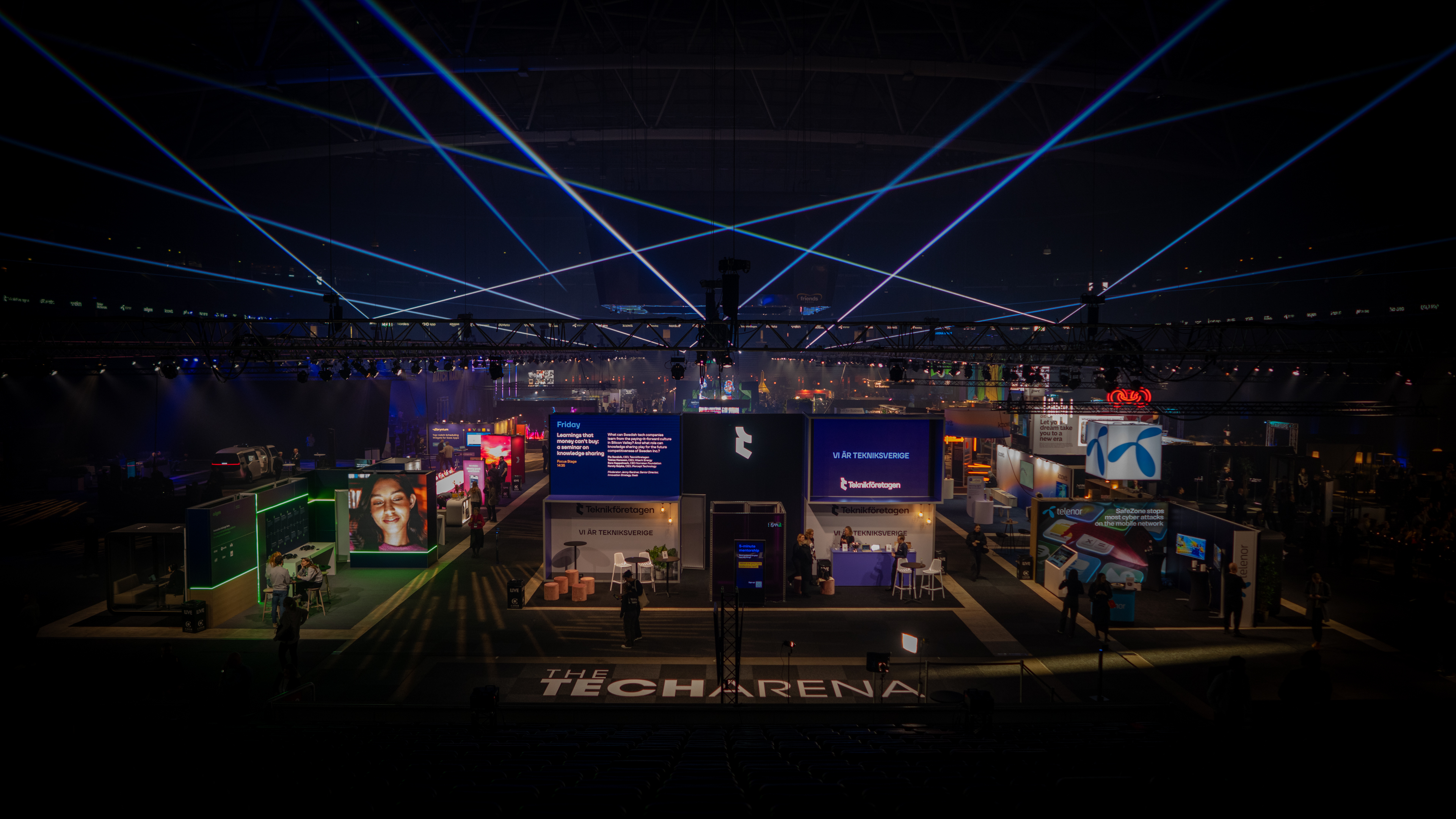 Wide view of the Tech Arena venue with blue beam lighting over the expo floor and stands