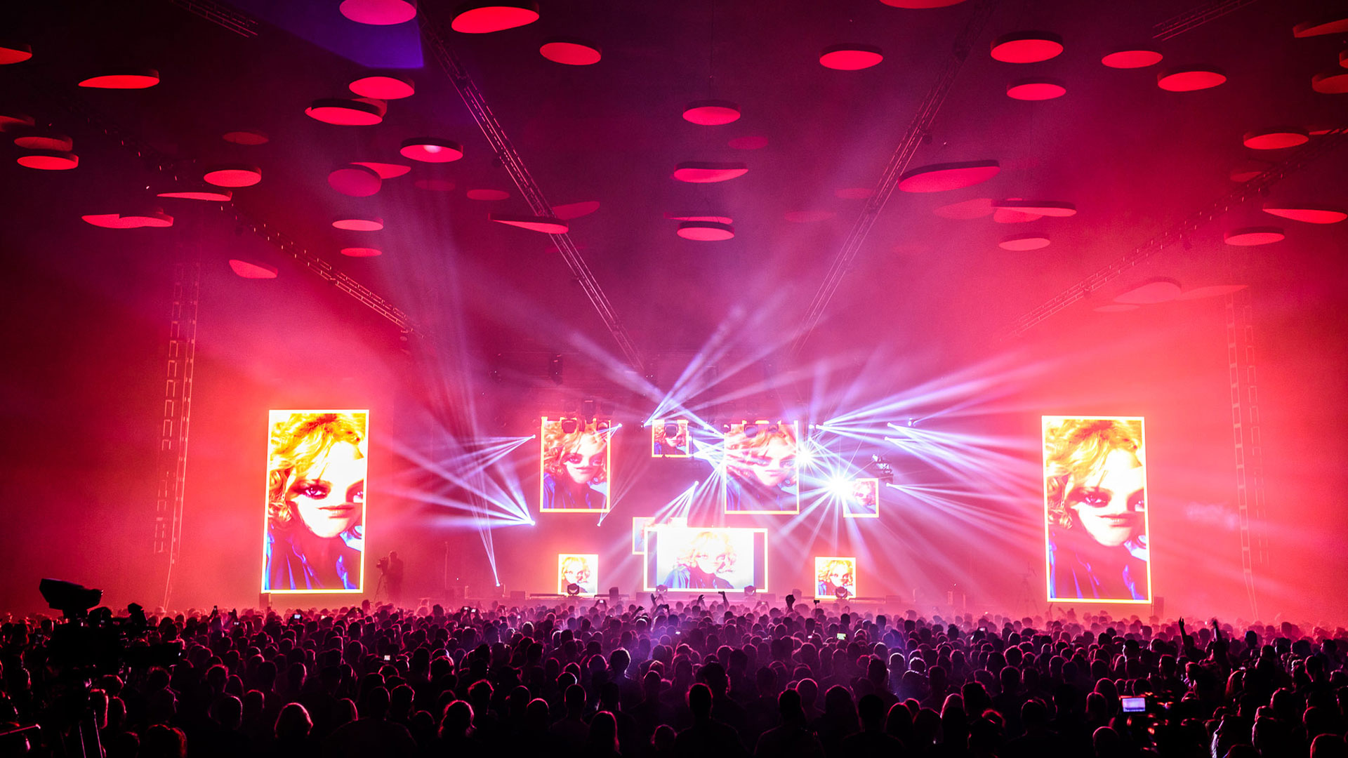 Concert stage at Flow Festival lit in pink and red, with screens showing the performer, beams of light and red discs on the ceiling above a packed crowd