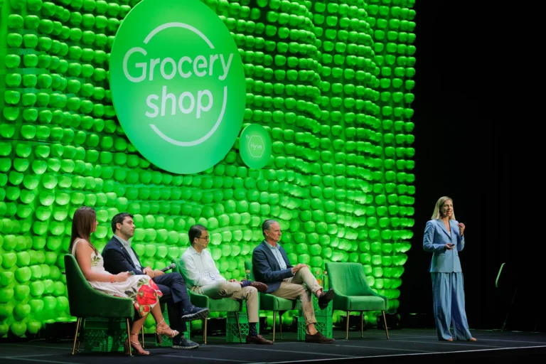 Groceryshop stage with a backdrop of thousands of green apples, an orange ‘Grocery shop’ sign and a panel of speakers
