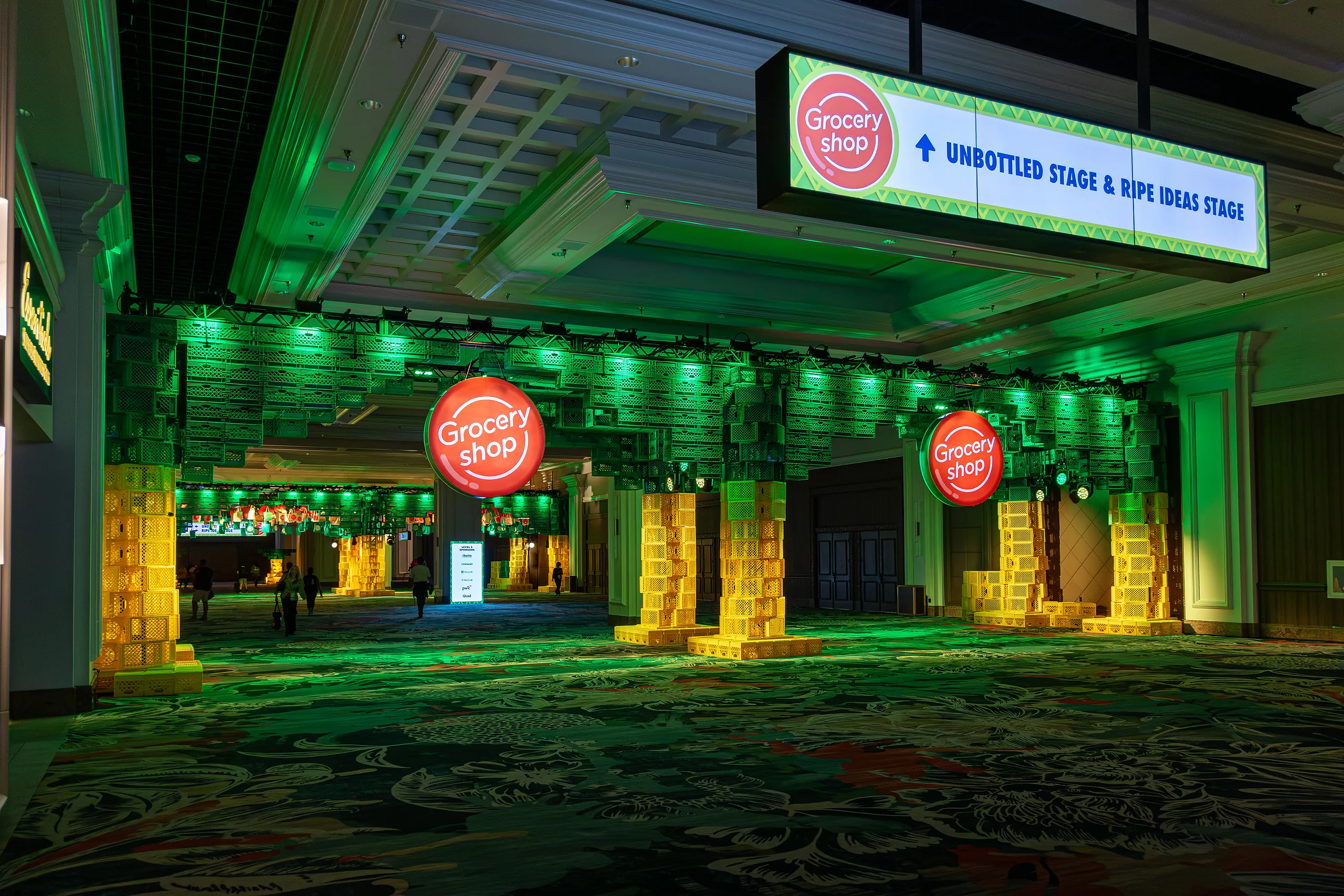 Entrance hall at Groceryshop with columns uplit in green, an orange ‘Grocery shop’ sphere and an overhead sign