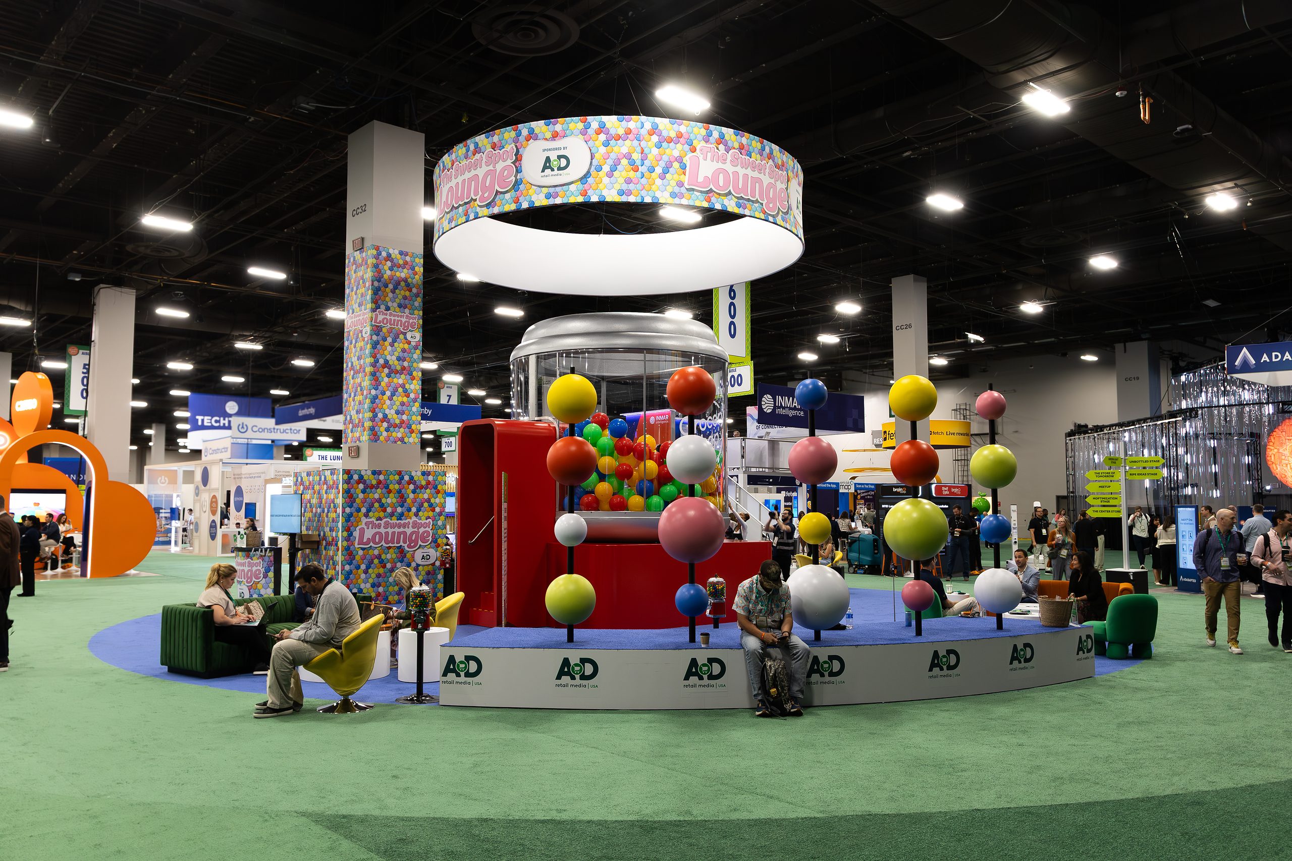 Colourful Groceryshop expo stand with a circular overhead sign, hanging spheres and product displays