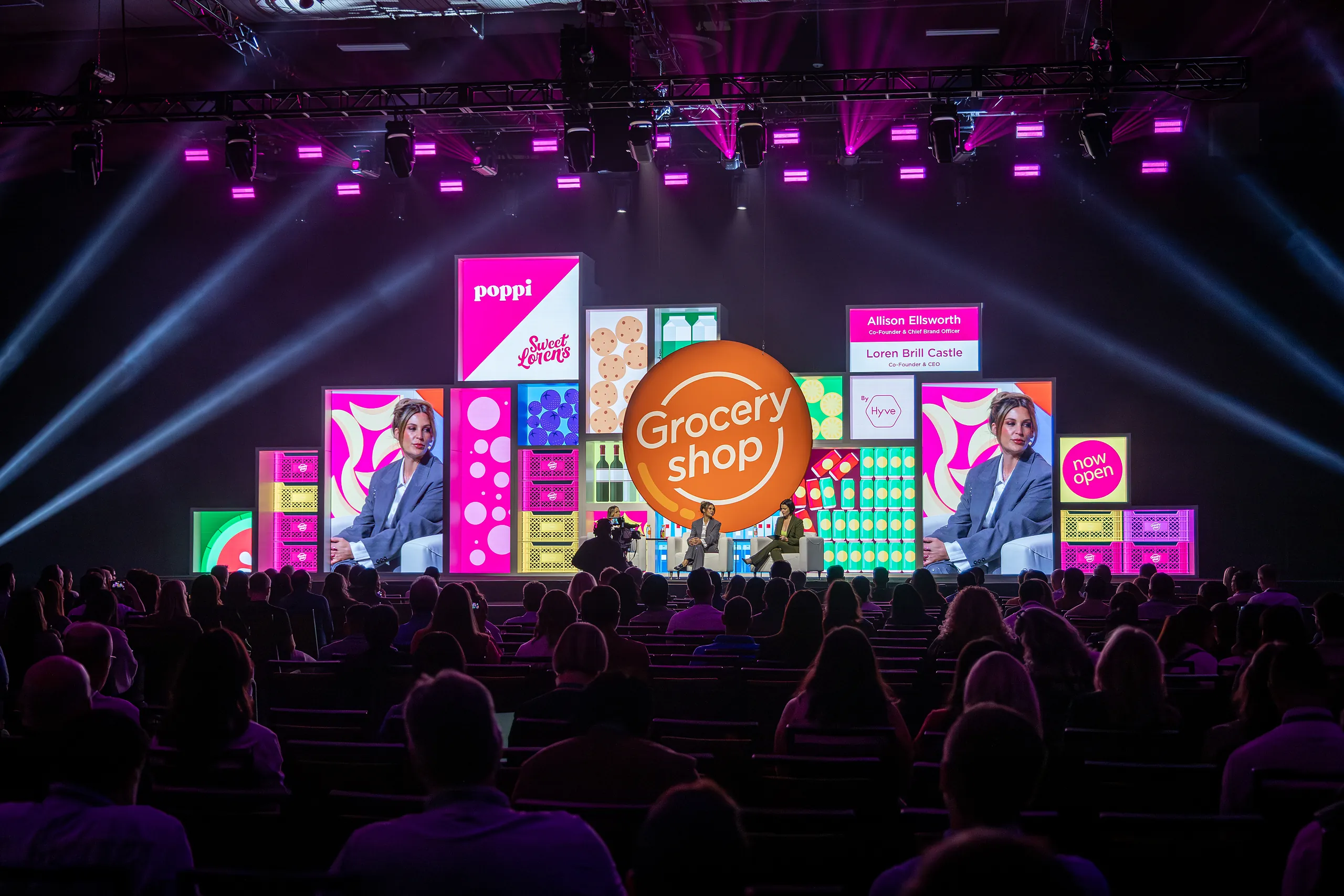 Wide view of the Groceryshop main stage under magenta lighting, with a modular product-box backdrop and an orange ‘Grocery shop’ sphere