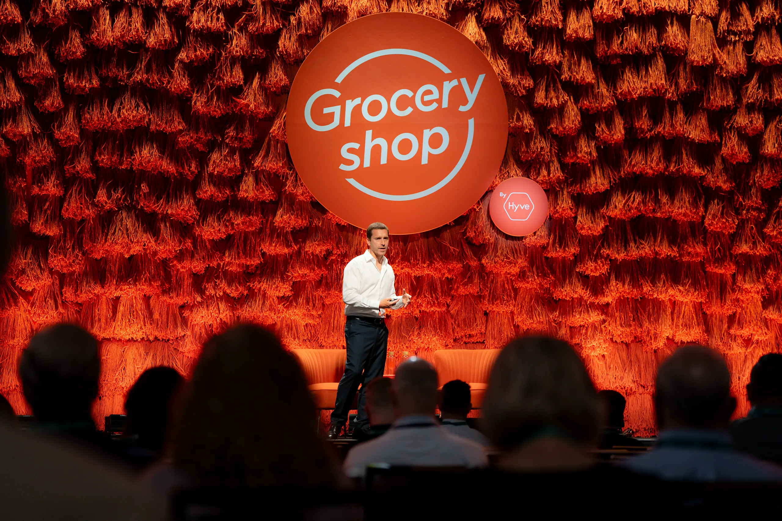 Groceryshop stage with a deep-red textured backdrop and an orange ‘Grocery shop’ sphere as a speaker presents