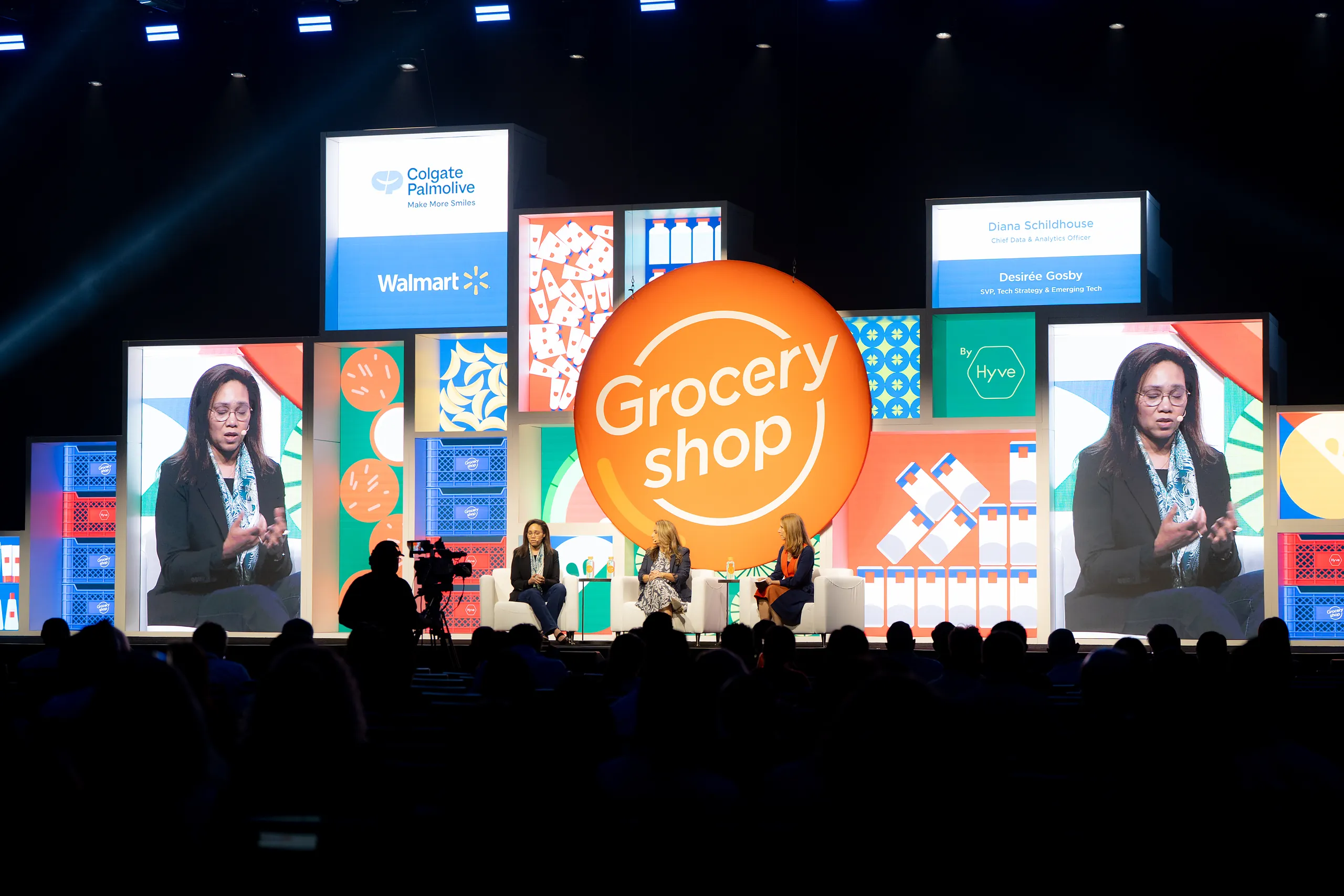 Panel discussion at Groceryshop with speakers on stage in front of a modular backdrop of product-box graphics and a large orange ‘Grocery shop’ sphere
