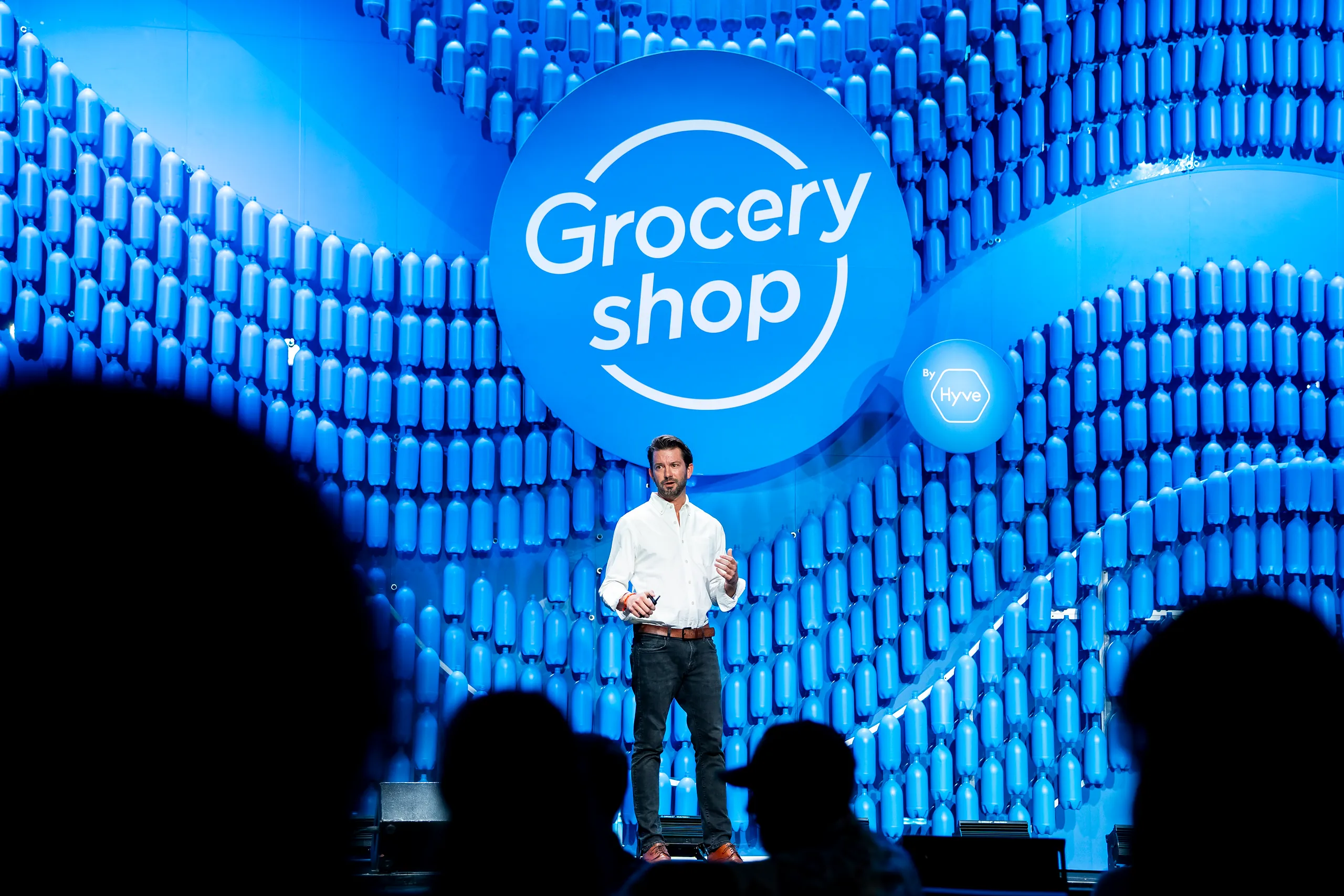 Groceryshop stage backed by a wave of blue plastic bottles, with an orange ‘Grocery shop’ sphere and a speaker