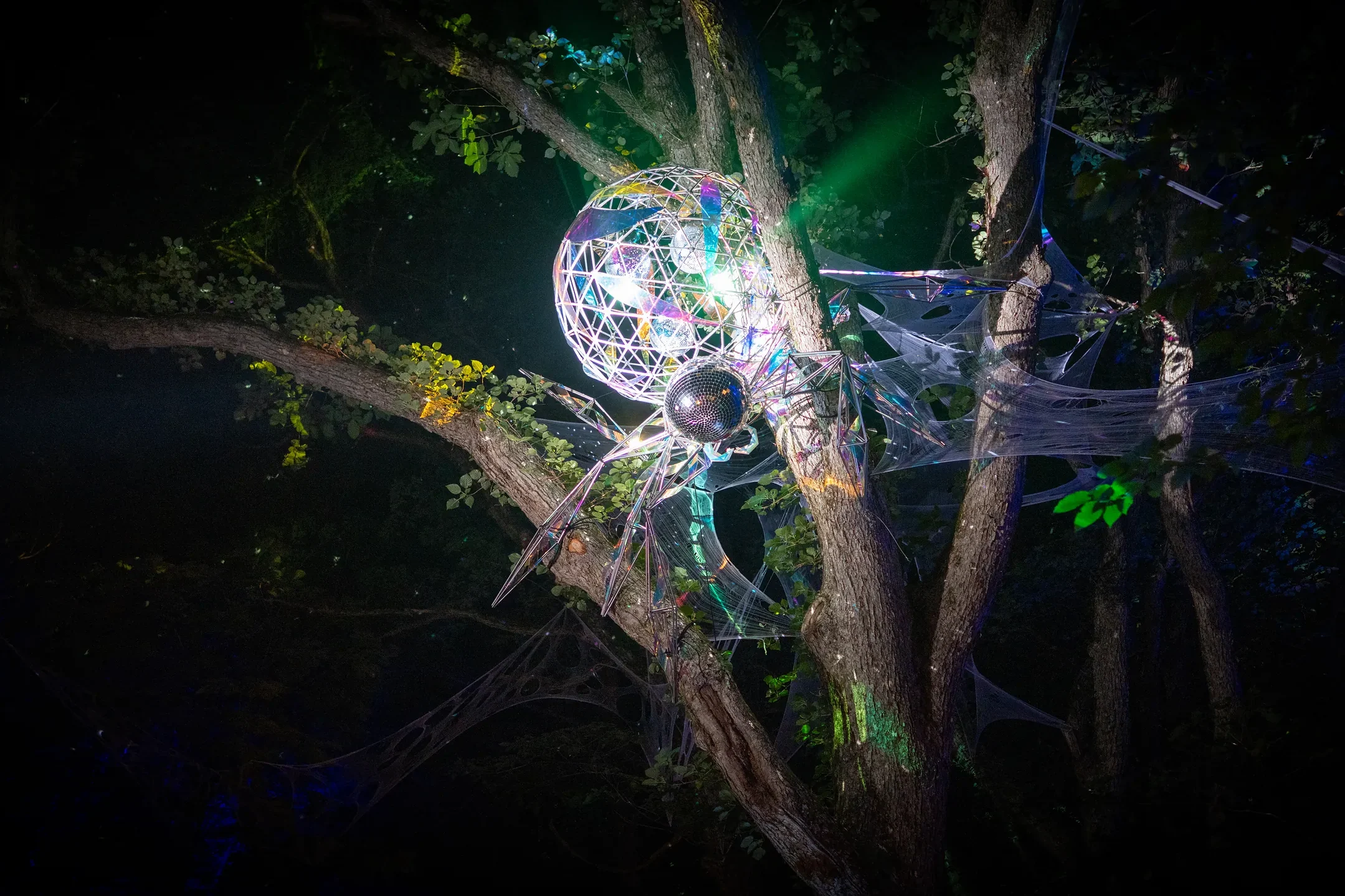 Faceted mirror-ball installation hanging in a tree, reflecting light across the Fuji Rock forest at night