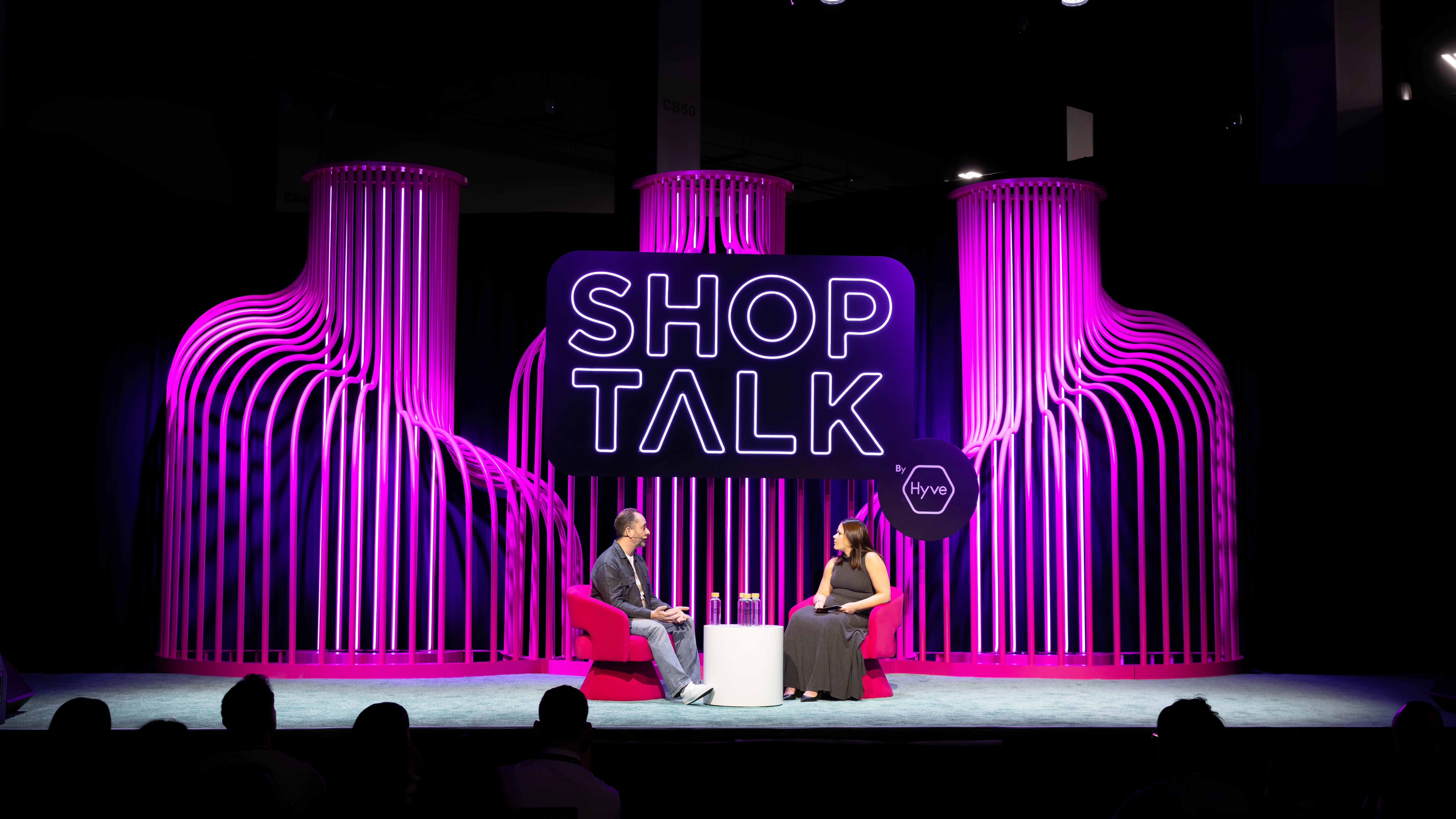 Shoptalk stage with tall fluted columns lit magenta and a ‘SHOP TALK’ logo, two people in conversation